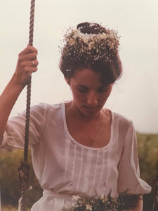 photograph of a beautiful bride sitting on a swing with a halo of flowers and a white cotton dress.